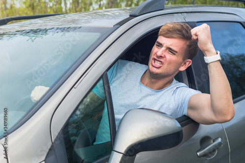 Fotografie Angry aggressive guy, young emotional irritated man driver screaming, shouting, yelling while driving car, threatening with a fist from automobile window