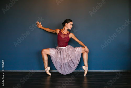 Modern ballet dancer performing ballet exercise on dark studio background. Dancer in a burgundy burgundy swimsuit