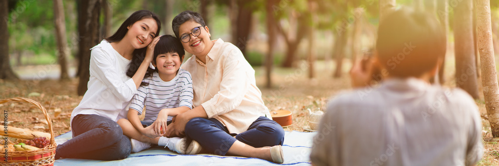 Panoramic banner image of happy Asian family in the garden taking a photograph with natural sunlight, Happy moment time in the park with grandma.