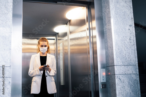 Business woman wearing protective white face mask is using elevator