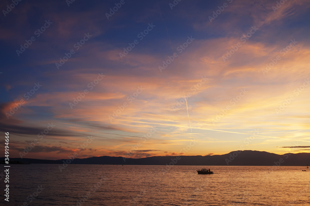 Silhouette of lonely boat in the sunset with dramatic sky. High seas sunset with a fishing ship on the horizon.