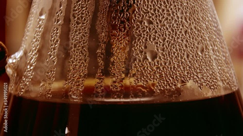 dark brown and golden coffee dripping with bubbles in a decanter as drops of fresh coffee drips out of the paper coffee filter. Steam collects on the sides of the walls glass carafe. 