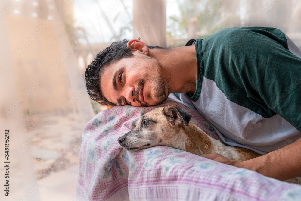 hombre joven y perro domestico, apoyan sus cabezas sobre el respaldo de un sillon en el jardin y sonrien. hombre joven y perro domestico, apoyan sus cabezas sobre el respaldo de un sillon en el jardin y sonrien.