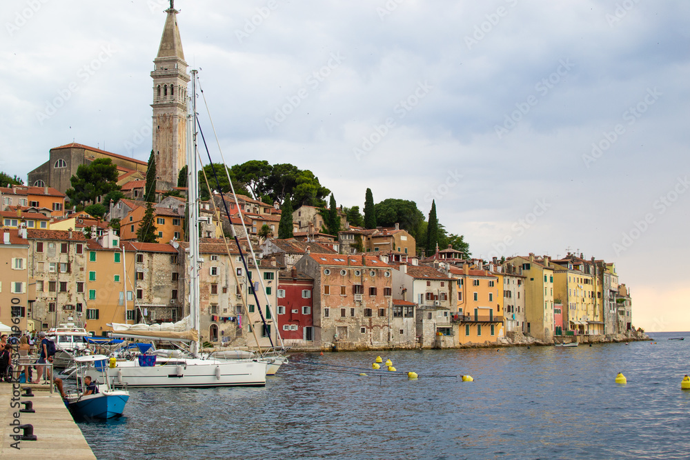View of the typical croatian houses in the coastline of the old town of Rovinj, Croatia, with some boats on the left and the tower of the Church of St Euphemia on the top