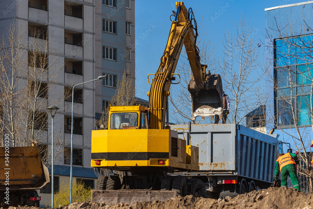 Excavator loader and dump truck during earthworks at a construction site. Loading land in the back of a heavy truck. Excavator digs land for the construction of a new park area. Excavator loader and dump truck during earthworks at a construction site. Loading land in the back of a heavy truck. Excavator digs land for the construction of a new park area.