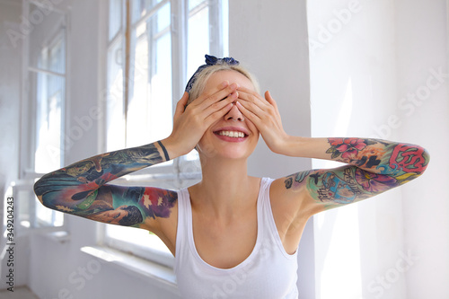 Foto Glad good looking young blonde female with tattoos holding palms on her eyes and