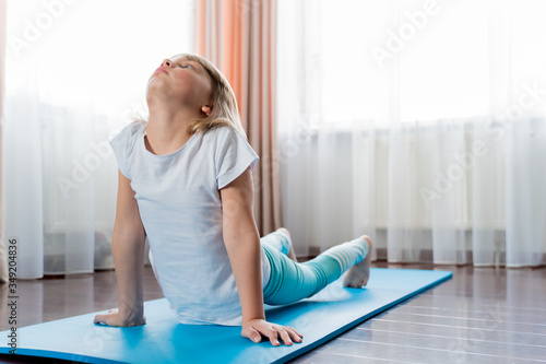 Little girl make home workout in flat. Baby yoga,fitness training, gymnastics, stretching. Distance school physical morning exercises on blue mat. Healthy activity,fun.Quarantine,coronavirus,covid-19