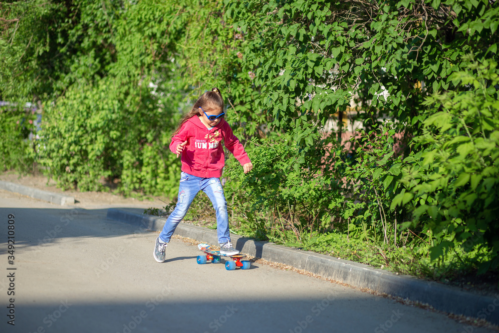 Obraz premium Little Girl in jeans and sunglasses rides a skateboard around the yard