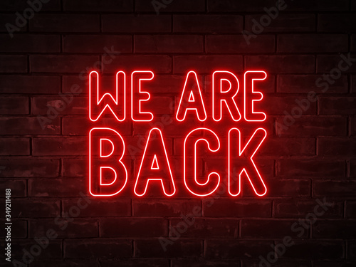 We are back - red neon light word on brick wall background 