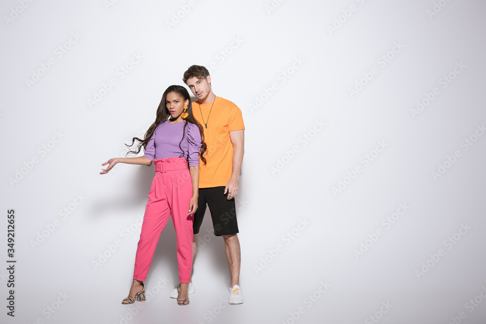 full length view of trendy african american girl standing with open arm near handsome boyfriend on white background