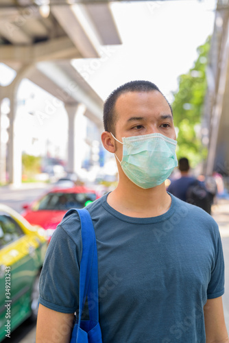 Young Asian man with mask for protection from corona virus outbreak at the taxi station in the city