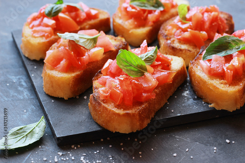 Italian appetizer bruschetta with tomatoes and basil on a black board close up.