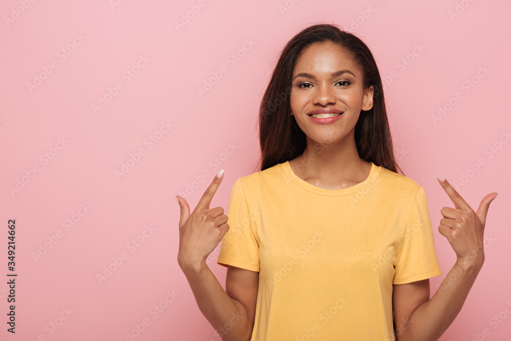 smiling african american girl pointing with fingers at braces on her teeth isolated on pink smiling african american girl pointing with fingers at braces on her teeth isolated on pink