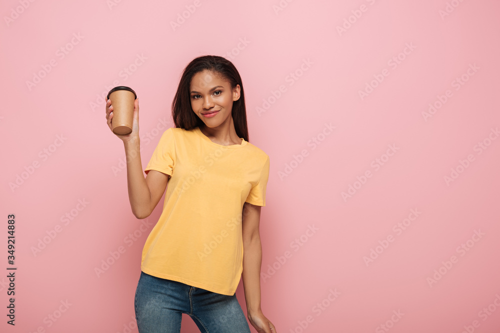 happy african american girl looking at camera while holding coffee to go on pink background happy african american girl looking at camera while holding coffee to go on pink background