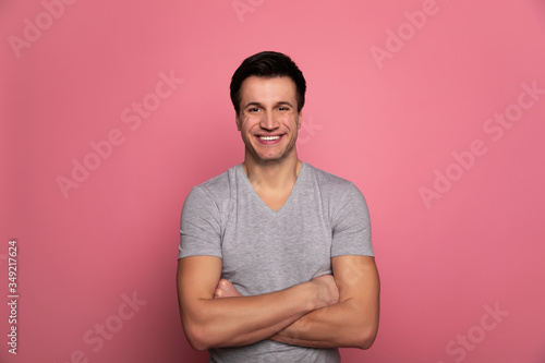 Frendliness. Close-up photo of a confident man in casual clothes, who is standing with folded arms, looking in the camera snd smiling.