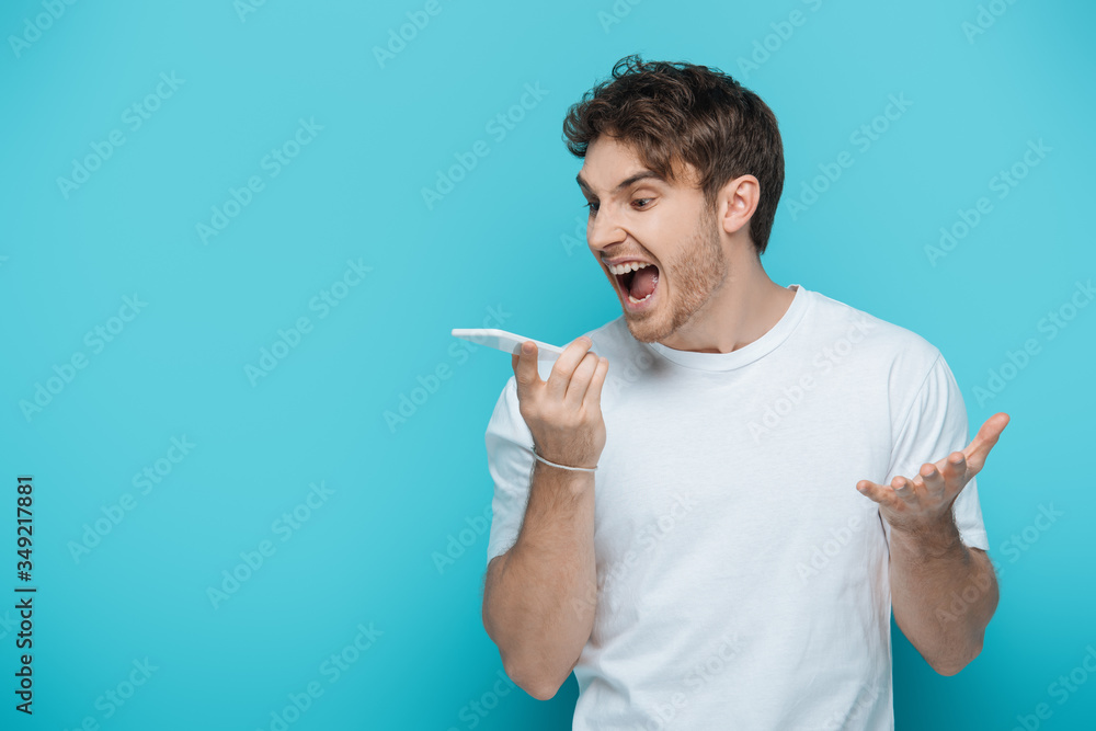 angry young man shouting during video call on blue background angry young man shouting during video call on blue background