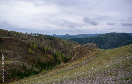 Mountain landscape. Valleys covered with green grass. Mixed forest. Rocky ledges. Sky with clouds.