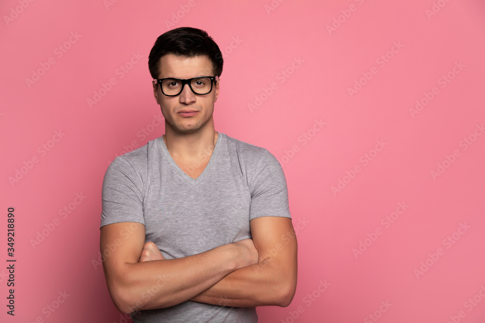 Smart and strong.Close-up photo of a handsome man in a grey t-shirt and glasses, who is looking in the camera while standing with folded arms. Smart and strong.Close-up photo of a handsome man in a grey t-shirt and glasses, who is looking in the camera while standing with folded arms.