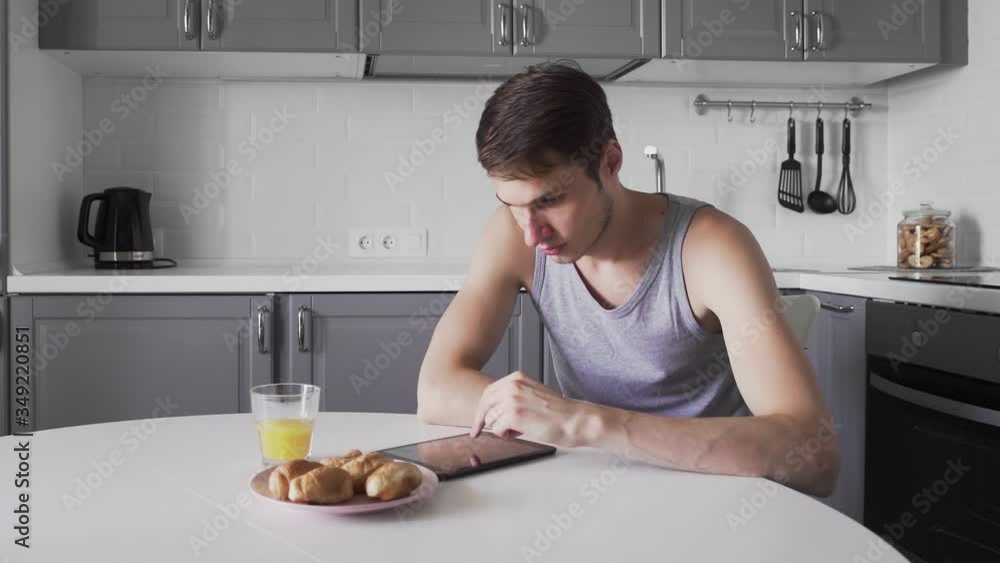 Young man using digital tablet while sitting in kitchen at home Young man using digital tablet while sitting in kitchen at home