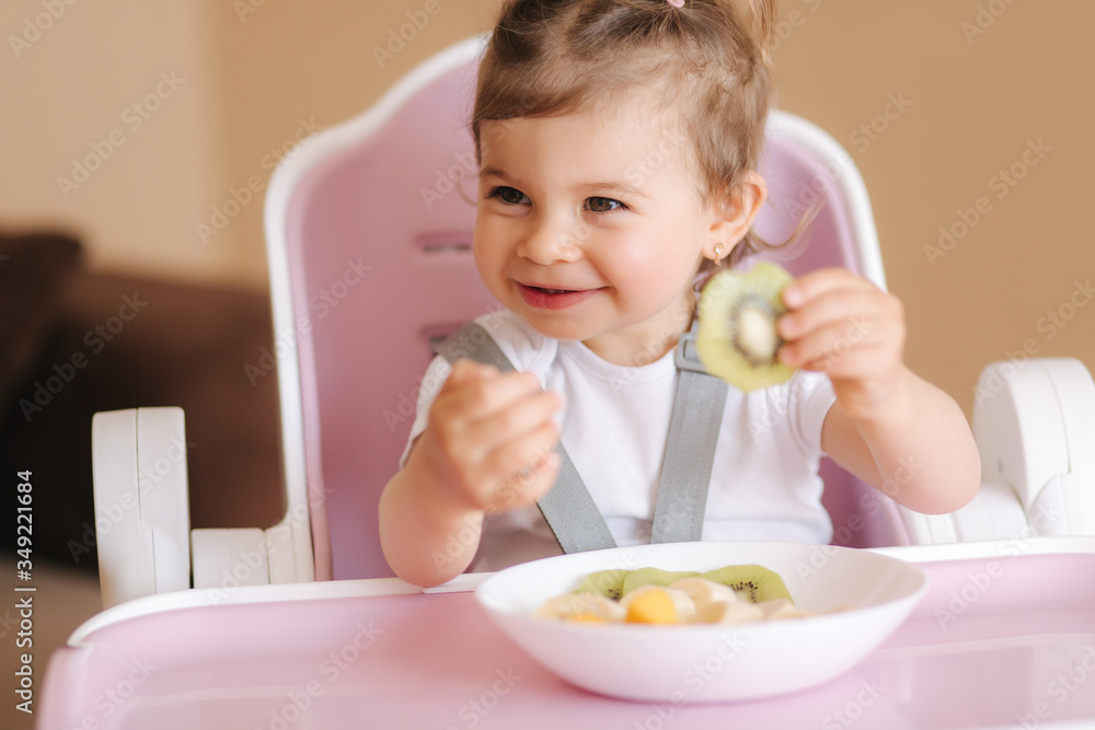 Portrait of happy little kid eating kiwi in high chair. Healthy nutrition for kids Portrait of happy little kid eating kiwi in high chair. Healthy nutrition for kids