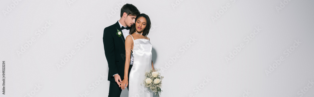horizontal image of elegant interracial newlyweds standing with closed eyes on white background horizontal image of elegant interracial newlyweds standing with closed eyes on white background