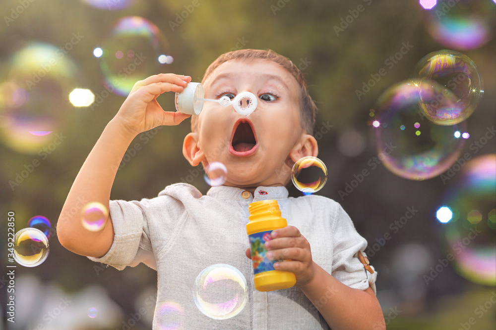 A child with an open mouth and big eyes blows colorful soap bubbles in nature.