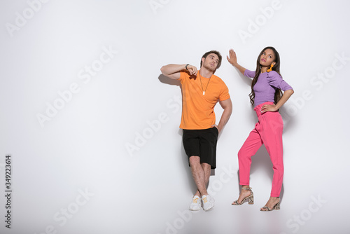 full length view of young, stylish interracial couple in bright clothes posing on white background