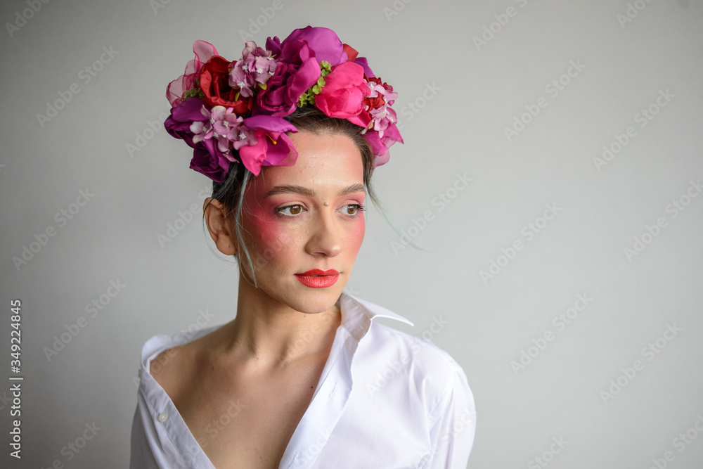 Naklejka premium Sensual woman in floral wreath. Portrait of beautiful young woman with red lips dressed in a white blouse.