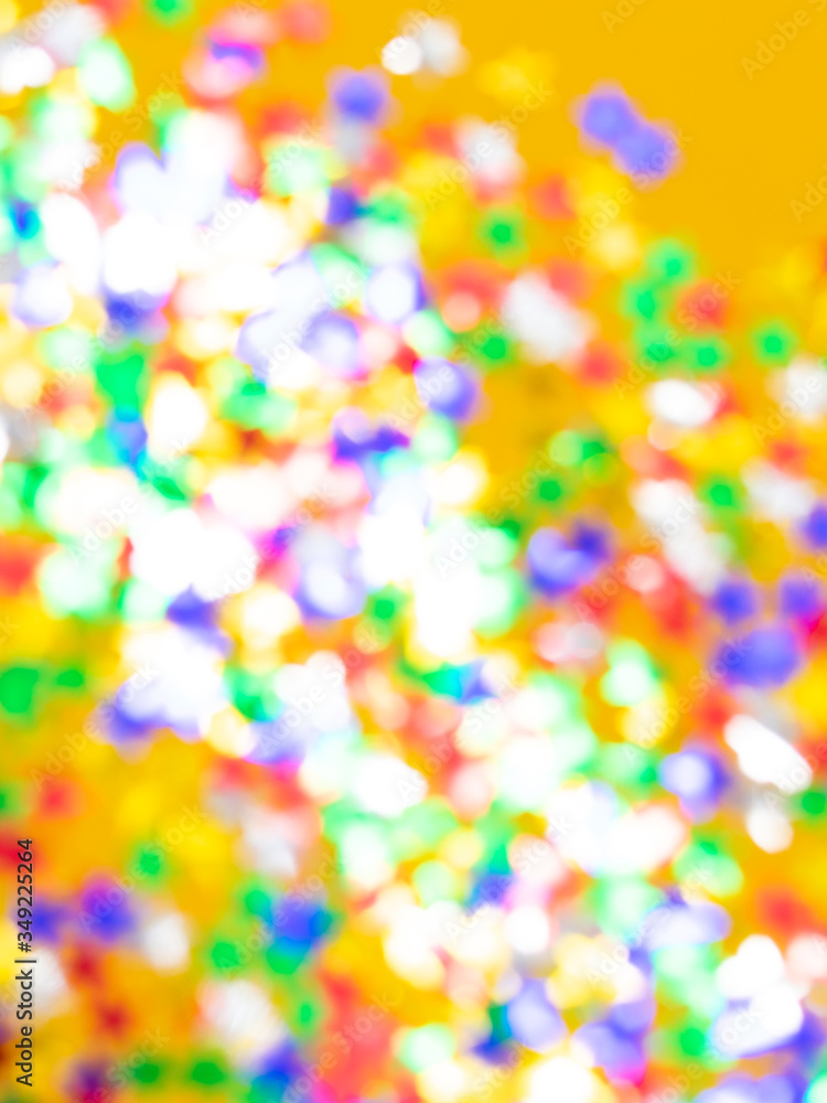 Blurred background with multicolored sparkles and lights on a yellow background