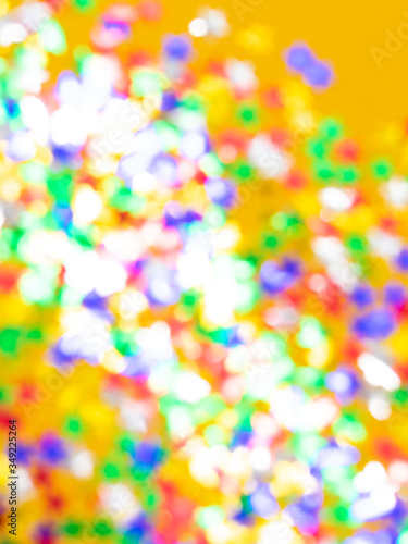 Blurred background with multicolored sparkles and lights on a yellow background