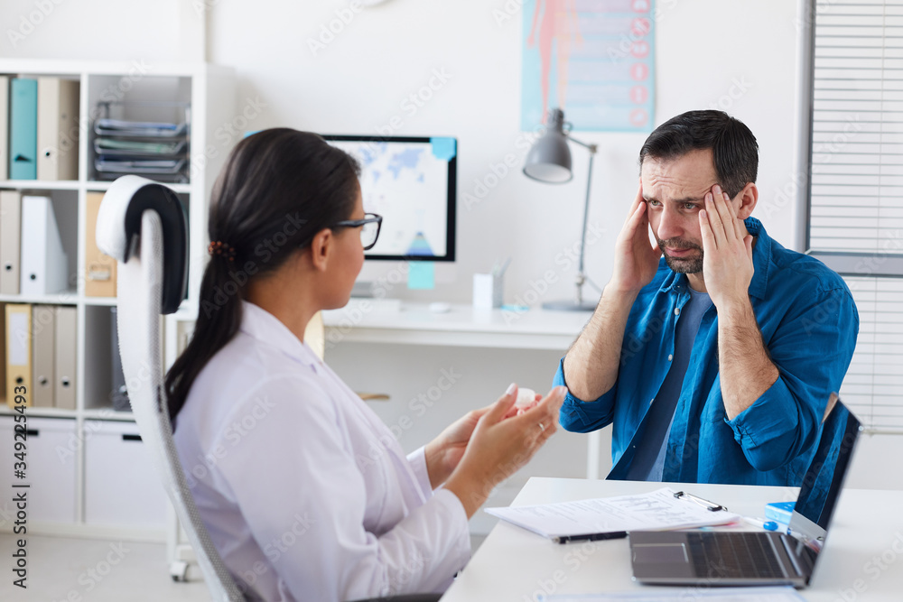 Patient complaining on headache during his visit to the doctor while doctor prescribing him the medicine Patient complaining on headache during his visit to the doctor while doctor prescribing him the medicine