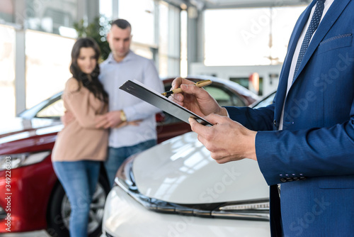 Dealer hands with clipboard and happy family behind