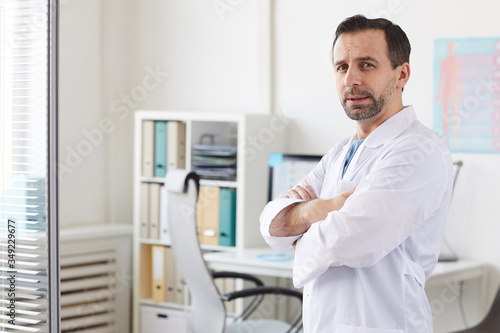 Portrait of male doctor in white coat standing with his arms crossed and looking at camera at hospital