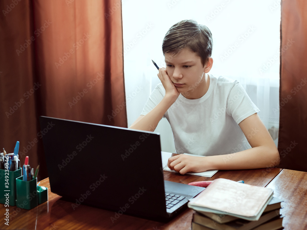 Student looking at computer, watching online education classes or webinar at home. Schoolboy studying with laptop and doing school homework. Distance and e-learning education concept, online lessons Student looking at computer, watching online education classes or webinar at home. Schoolboy studying with laptop and doing school homework. Distance and e-learning education concept, online lessons