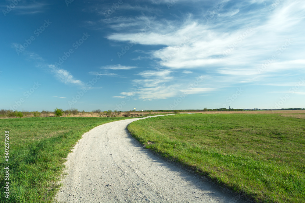 A bend on a gravel road and green meadows, white clouds on a blue sky