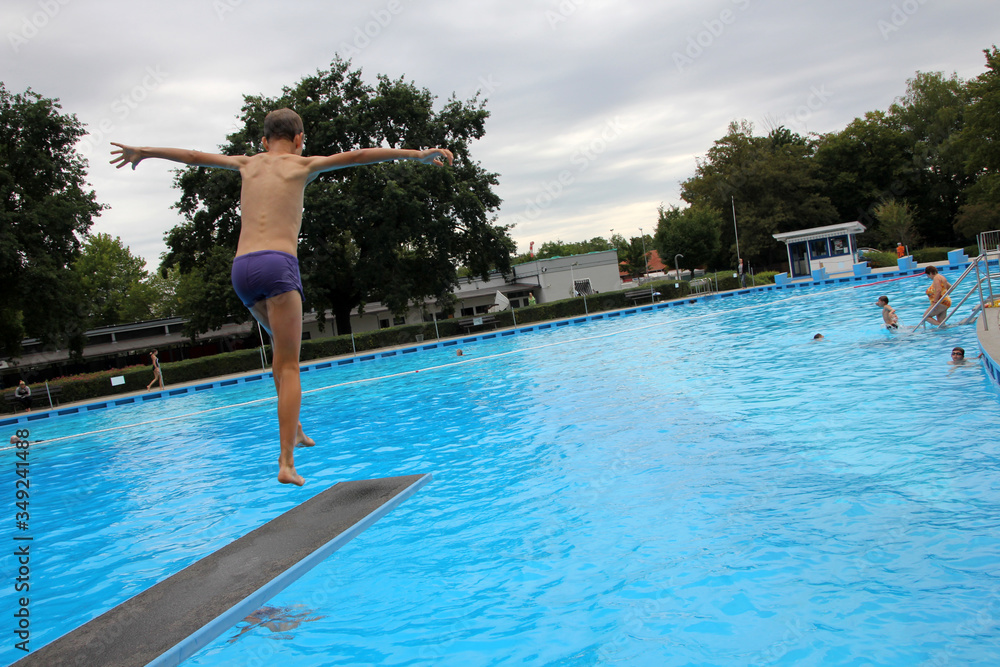 Ein Junge springt während den Sommertagen in einem Freibad vom Sprungbrett.