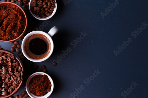 Fresh espresso cup, roasted and ground beans in clay bowls on dark blue table surface. Close-up, top view, copy space. Coffee shop, morning, baristas workplace concept