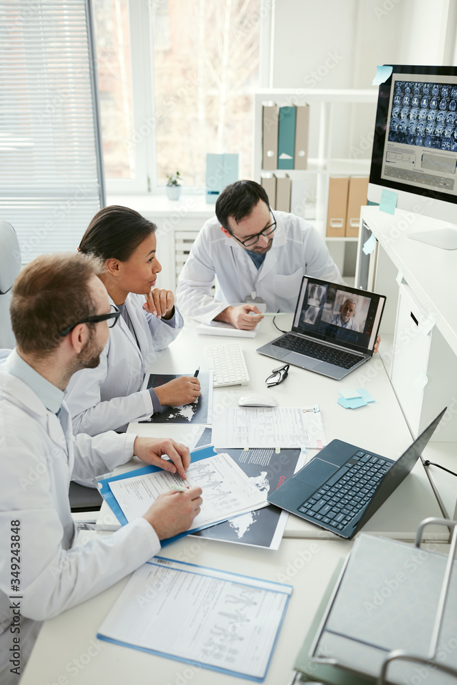 Obraz premium Group of doctors sitting at the table and talking to their colleague during online conference at meeting
