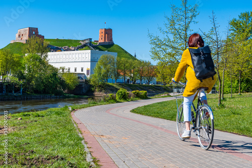 Girl or woman cycling on the road bike with park, river and castle on background during Covid or Coronavirus emergency, sustainable transport concept