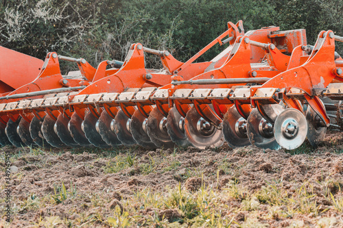 A red modern harrow stands in a field before sowing. Hydraulic mechanism for grinding the soil after plowing. © Niko_Dali