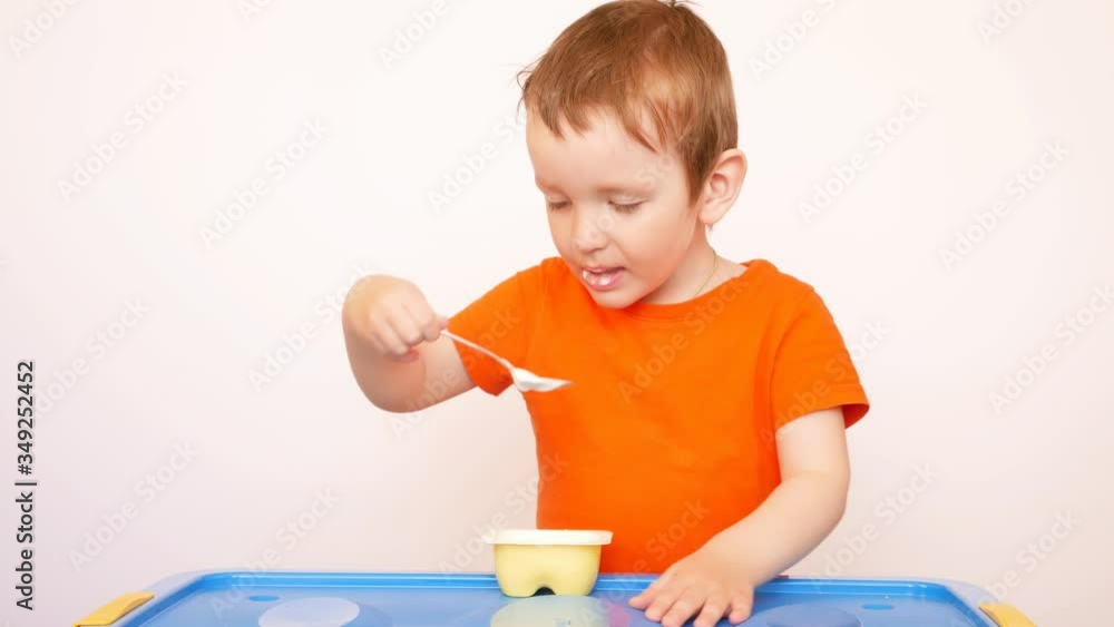 A cute little boy eating yogurt with a spoon A cute little boy eating yogurt with a spoon