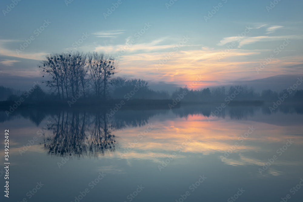 Sunset and clouds over a misty lake, trees on the horizon