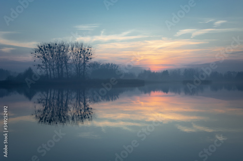 Sunset and clouds over a misty lake, trees on the horizon © darekb22
