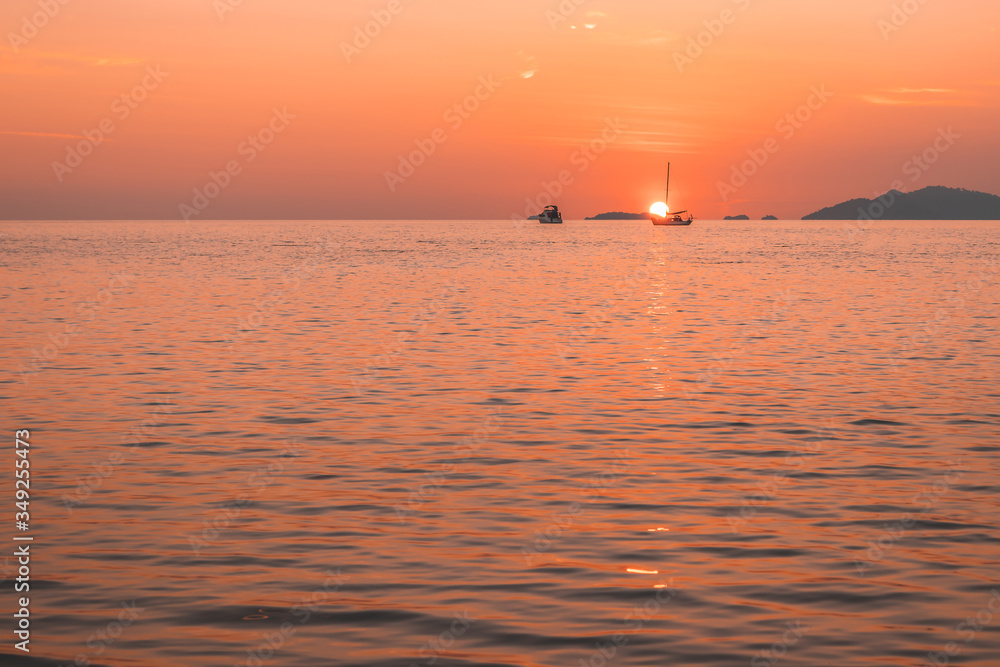 romantic sunset at sea with sailboat sailing along its journey against orange and yellow color filled sky