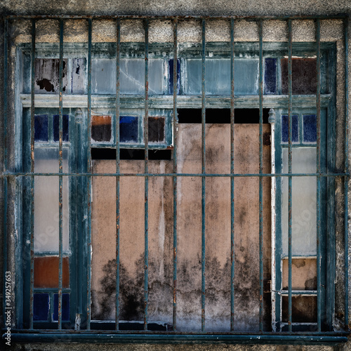 Fenêtre munie de barreaux avec des carreaux mulicolors et des planches de bois pour la condamner