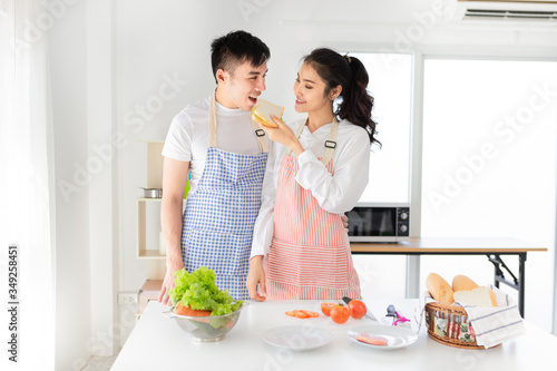 asian man and asian woman eating meal in the morning  they have breakfast in kitchen room  he holding hot coffee cup  she feed sandwich to her husband  they feeling happy  happiness honeymoon 