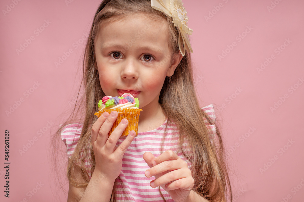 Cute little girl eating a cake on a pink background