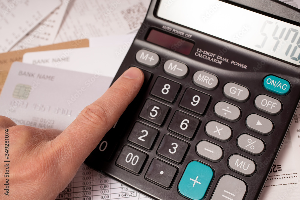 A finger on button of calculator with financial documents and credit cards under it A finger on button of calculator with financial documents and credit cards under it