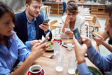 group of young caucasian people having unsocial lunch in restaurant, using their cell phones and not talking to each other. technology, social issues
