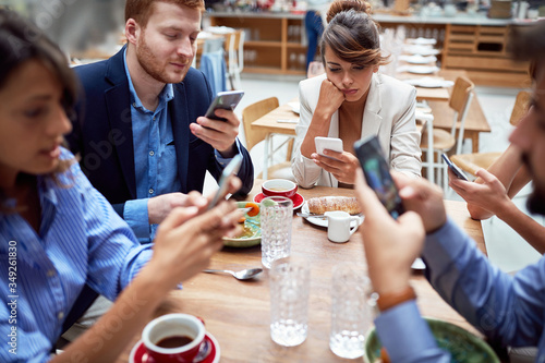 group of young caucasian people having unsocial lunch in restaurant, using their cell phones and not talking to each other. technology, social issues photo